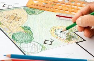 Hand drawing a colorful landscape design plan for an Aberdeen, MD project with pencils, templates, and ruler on a blueprint—crafted by Solid Brick Contracting.