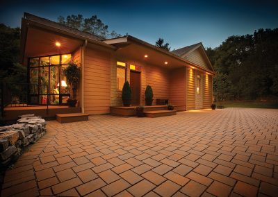 A warm, well-lit house in Aberdeen, MD with large windows and a spacious brick driveway at dusk—expertly crafted by Solid Brick Contracting.