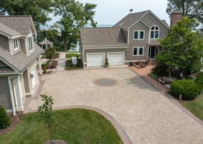 A large beige house in MD with a spacious paved driveway, garage, beautiful trees, and expertly designed landscaping around the property.