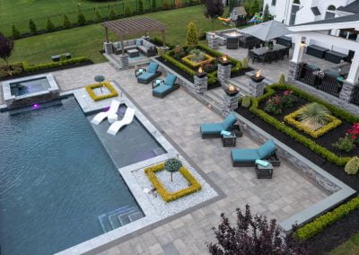Aerial view of a modern backyard in MD, expertly designed by Solid Brick Contracting, featuring a pool, lounge chairs, fire pits, and stunning landscaping.