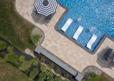 Aerial view of a pool with in-water lounge chairs, umbrellas, patio, and landscaped garden featuring expertly crafted hardscaping by Solid Brick Contracting in Aberdeen.