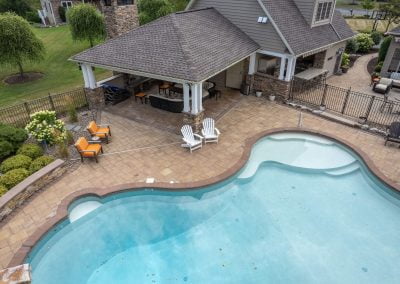 Aerial view of a beautifully landscaped backyard pool in Aberdeen, MD, featuring a patio with lounge chairs and a covered outdoor seating area by the house.