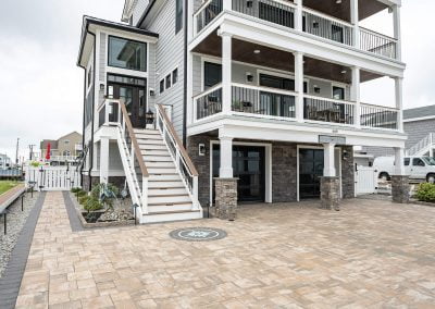 Three-story coastal house in Aberdeen with large balconies, white railings, and a wide stone driveway crafted by Solid Brick Contracting under a cloudy sky.