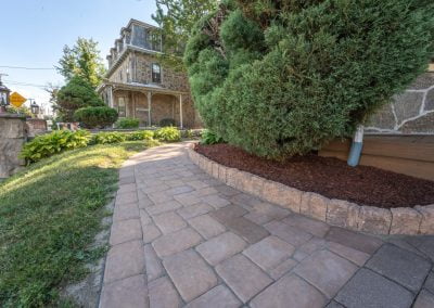 Curved stone walkway beside a house with shrubs, mulch, and green grass on a sunny day—expert hardscaping by Solid Brick Contracting in MD.