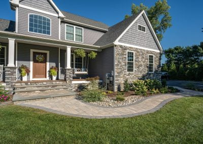Gray house with stone accents by Solid Brick Contracting, featuring a porch, potted plants, and elegant hardscaping with a curved stone walkway in a beautifully landscaped MD yard.