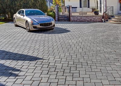 Silver sedan parked on a large, patterned stone driveway, showcasing expert hardscaping by Solid Brick Contracting, in front of an Aberdeen home with a black gate and brick steps.