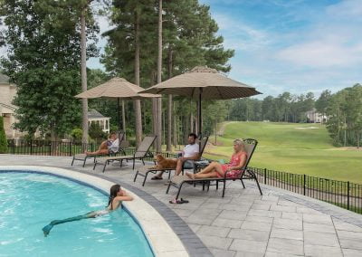 Three people relax on lounge chairs by a pool while another person swims, surrounded by beautiful landscaping and views of trees and a golf course in Aberdeen.
