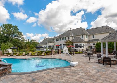 Luxury house in MD with a spacious backyard showcasing exquisite landscaping, a pool, patio seating, and lounge chairs under a partly cloudy sky.