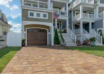 Three-story house in Aberdeen, MD, with balconies, an American flag, and a wide stone driveway under a blue sky—expertly crafted by Solid Brick Contracting.