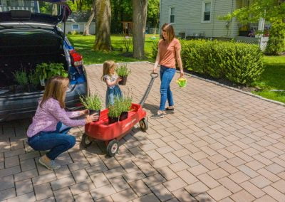 Two women and a girl load potted plants into a red wagon on the sunny driveway of their Aberdeen home, where Solid Brick Contracting recently completed beautiful hardscaping.