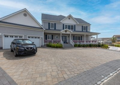 Two-story house in MD with patriotic bunting, beautiful landscaping, a black car parked in the driveway, and blue sky above.