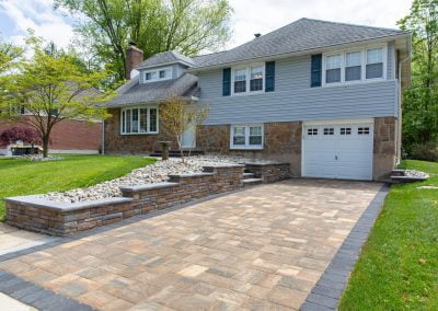 Two-story suburban house in MD featuring expert hardscaping with a stone driveway and retaining walls, plus a beautifully landscaped front yard with trees.