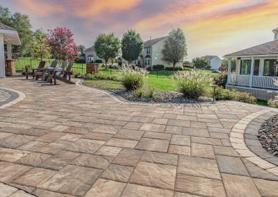 Enjoy a spacious patio with stone pavers, outdoor chairs, and lush landscaping at sunset under a colorful sky—crafted by Solid Brick Contracting in Aberdeen.