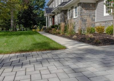 Modern house with gray siding and stone façade, paver walkway, and expert landscaping in the front yard by Solid Brick Contracting, MD, on a sunny day.