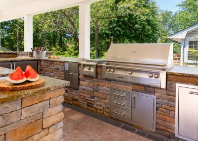 Outdoor kitchen by Solid Brick Contracting in Aberdeen, MD, featuring a stainless steel grill, sleek countertop, and a plate with sliced watermelon.