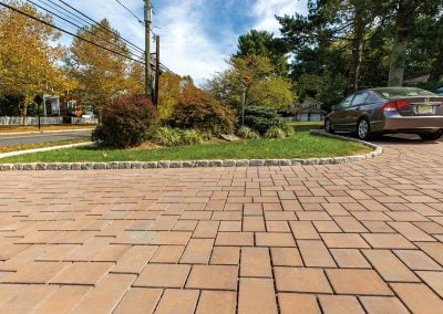 Brick paver driveway with a parked car, surrounded by grass, trees, and landscaped shrubs—expertly crafted by Solid Brick Contracting, your MD hardscaping professionals.