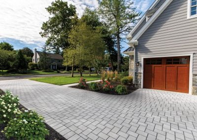 A modern house in Aberdeen with a gray brick driveway crafted by Solid Brick Contracting, wooden garage doors, and landscaped hardscaping garden beds.