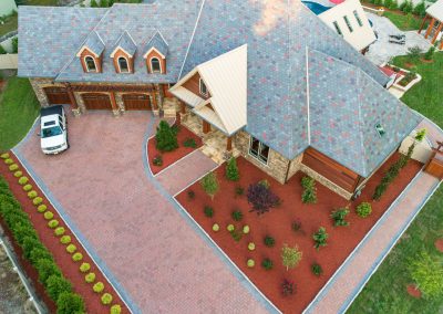 Aerial view of a large house in MD with a brick driveway by Solid Brick Contracting, landscaped yard, and white vehicle parked outside.