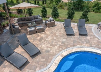 Poolside patio with lounge chairs, sofa set, umbrella, and lush landscaping in the background on a sunny day—perfect for relaxing outdoors in MD.