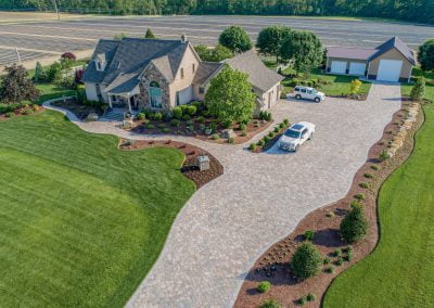 Aerial view of a large MD home with beautiful landscaping, curving driveway, and two white cars near farm fields—quality you’d expect from Solid Brick Contracting.