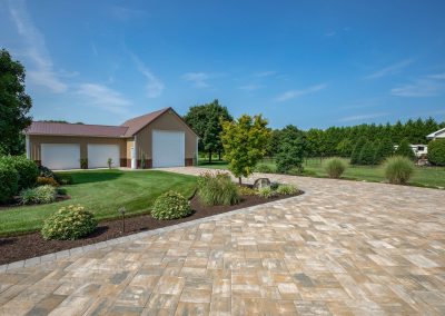 Large paved driveway leads to a beige garage, surrounded by expert landscaping and lush green lawn under a blue sky—crafted with care by Solid Brick Contracting.