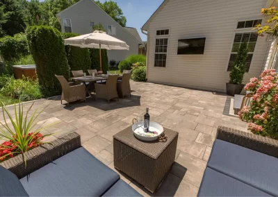 Spacious stone patio with outdoor dining set, umbrella, wicker seating, and a tray with wine and glasses—perfect for Aberdeen, MD homes seeking stylish landscaping upgrades.