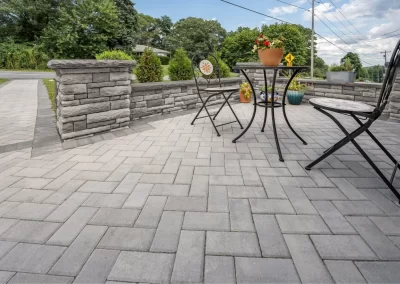 Patio with gray paver stones, black metal table and chairs, potted flowers, and a stone wall in the background creates stunning hardscaping perfect for Aberdeen landscaping.