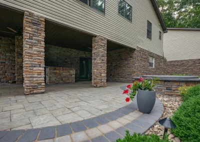 Spacious stone patio with large columns, potted red flowers, and a beautifully landscaped garden by Solid Brick Contracting, MD, near a house.