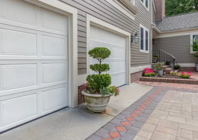Two white garage doors with potted topiary and a patterned hardscaping stone driveway enhance this Aberdeen, MD home’s curb appeal.