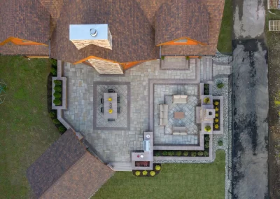 Aerial view of a beautifully landscaped stone patio with dining and lounge areas behind a brown-roofed house, expertly crafted by Solid Brick Contracting in MD.