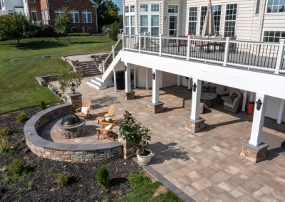 Spacious backyard patio in Aberdeen, MD, featuring elegant hardscaping with a fire pit, Adirondack chairs, and a covered seating area under a raised deck.