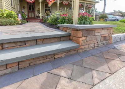 Stone steps and a stone retaining wall, crafted by Solid Brick Contracting, lead to an Aberdeen house adorned with flowers and charming garden decorations—an inviting touch of expert landscaping.