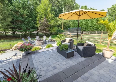 Backyard patio in Aberdeen featuring stylish hardscaping with wicker chairs, a yellow umbrella, and a cozy fire pit area surrounded by Adirondack chairs.