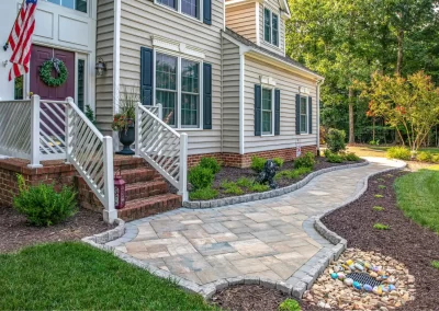 A stone walkway curves to a house in Aberdeen, MD, featuring brick steps, hardscaping accents, garden beds, and painted rocks by the path.