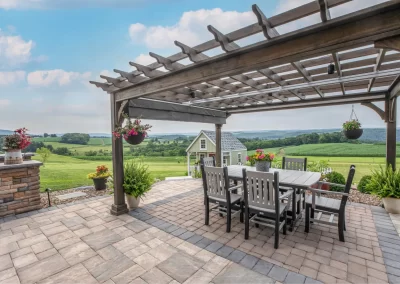 Patio with a pergola, dining table, and hanging plants by Solid Brick Contracting MD features beautiful hardscaping and overlooks a green field and distant hills.