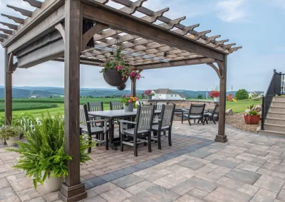 Wooden pergola over outdoor dining set on a paved patio, with potted plants and scenic landscape in the background—expertly crafted by Solid Brick Contracting, serving Aberdeen, MD.