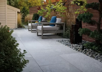 Modern patio in Aberdeen with two cushioned chairs, lush landscaping, and stone tiles, all enclosed by a wooden privacy fence—expertly crafted by Solid Brick Contracting.
