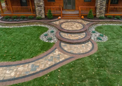 Circular stone steps and walkway with brick trim enhance the landscaped yard in front of a house with a porch. Expertly crafted by Solid Brick Contracting, this Aberdeen project showcases quality landscaping and classic curb appeal.