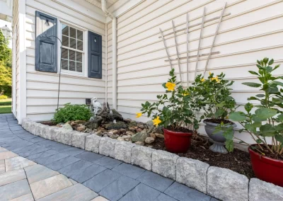 Curved stone walkway beside a garden bed with yellow flowers and a small rock fountain by a house, showcasing expert landscaping by Solid Brick Contracting in MD.