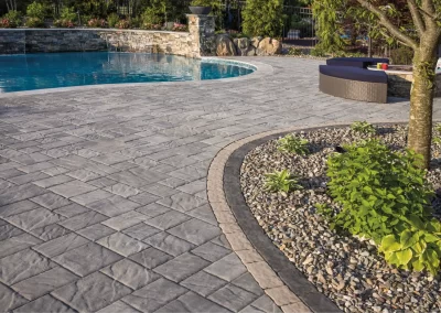 Poolside patio in Aberdeen featuring stone pavers, elegant hardscaping, curved landscaping, small plants, and round outdoor seating.