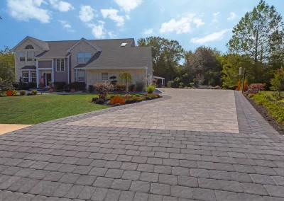 A large house with a wide stone paver driveway, expertly hardscaped by Solid Brick Contracting in MD, surrounded by green lawn and landscaped bushes.