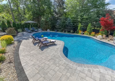 Curved backyard pool with lounge chairs and umbrellas, surrounded by trees, landscaped garden, and elegant hardscaping—an inviting outdoor oasis in Aberdeen, MD.