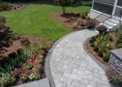 Curved stone walkway with surrounding flower beds and shrubs leading to a green lawn and a screened porch—expert hardscaping in Aberdeen, MD.