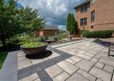 Spacious patio with modern hardscaping pavers, a large planter, outdoor chairs, and a brick house in the background—perfect for Aberdeen, MD living.
