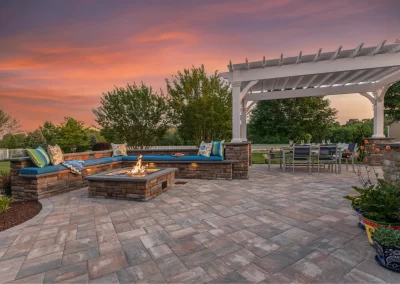 Stone patio with built-in fire pit, seating, and pergola, set against a colorful sunset sky—expert hardscaping in Aberdeen, MD.