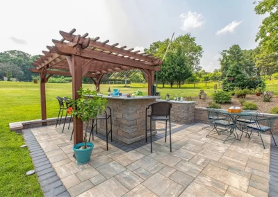Outdoor patio in a green Aberdeen backyard garden features a pergola, bar seating, potted plant, metal table set, and expert hardscaping by Solid Brick Contracting.