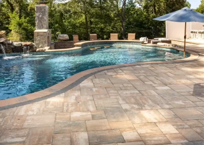 Curved swimming pool with stone patio, lounge chairs, umbrella, and trees in the background—expert landscaping brings a touch of Aberdeen, MD charm to this inviting outdoor oasis.