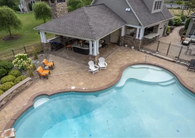 A backyard pool with hardscaping by Solid Brick Contracting, featuring a patio, lounge chairs, and a covered outdoor seating area near a house in MD.