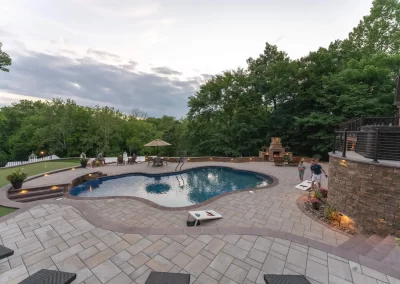 Backyard patio with a pool, people socializing, fireplace, cornhole game, and beautiful landscaping by Solid Brick Contracting in Aberdeen at sunset.