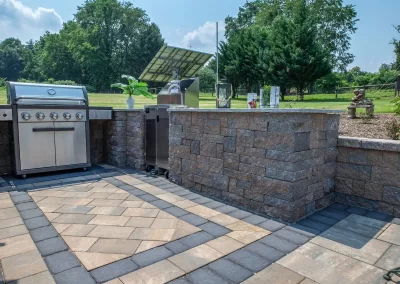 Outdoor kitchen in Aberdeen, MD featuring a stainless steel grill, stone counter, and patio overlooking a green yard with trees—crafted by Solid Brick Contracting.